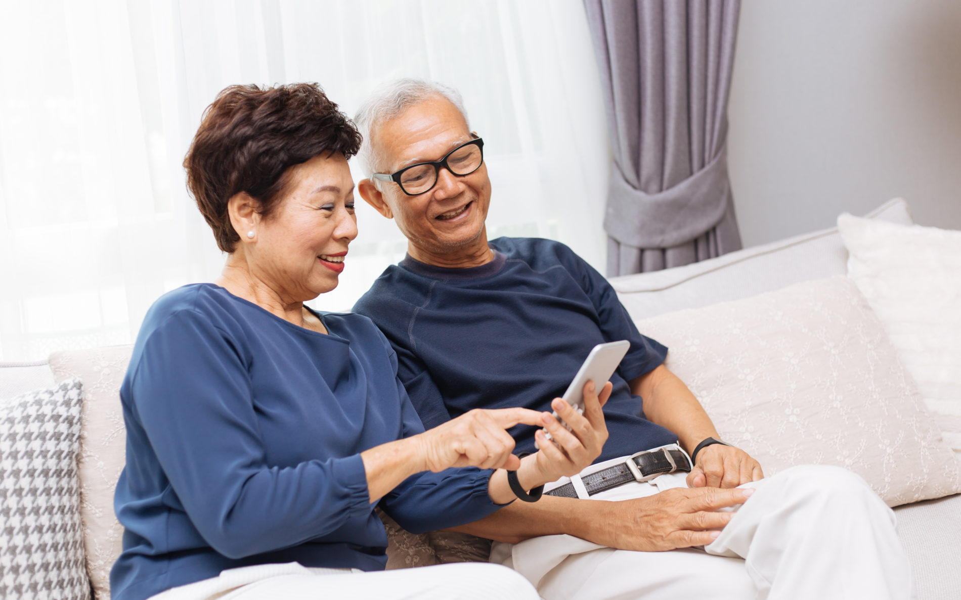 Senior Asian couple grandparents using a smart phone together on sofa at home