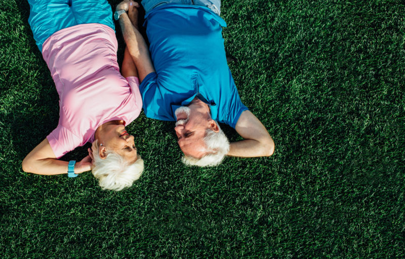 Senior couple laying in grass, top view. Elderly man and woman lying on grass together and hold their hands